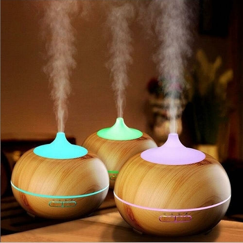 Three wooden diffusers with colorful lids emitting steam on a wooden surface.