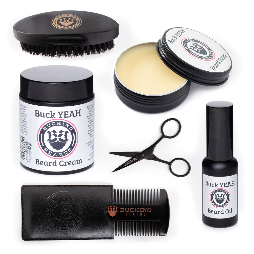 Collection of Buck Yeah beard care products including cream, oil, comb, and scissors on a white background.