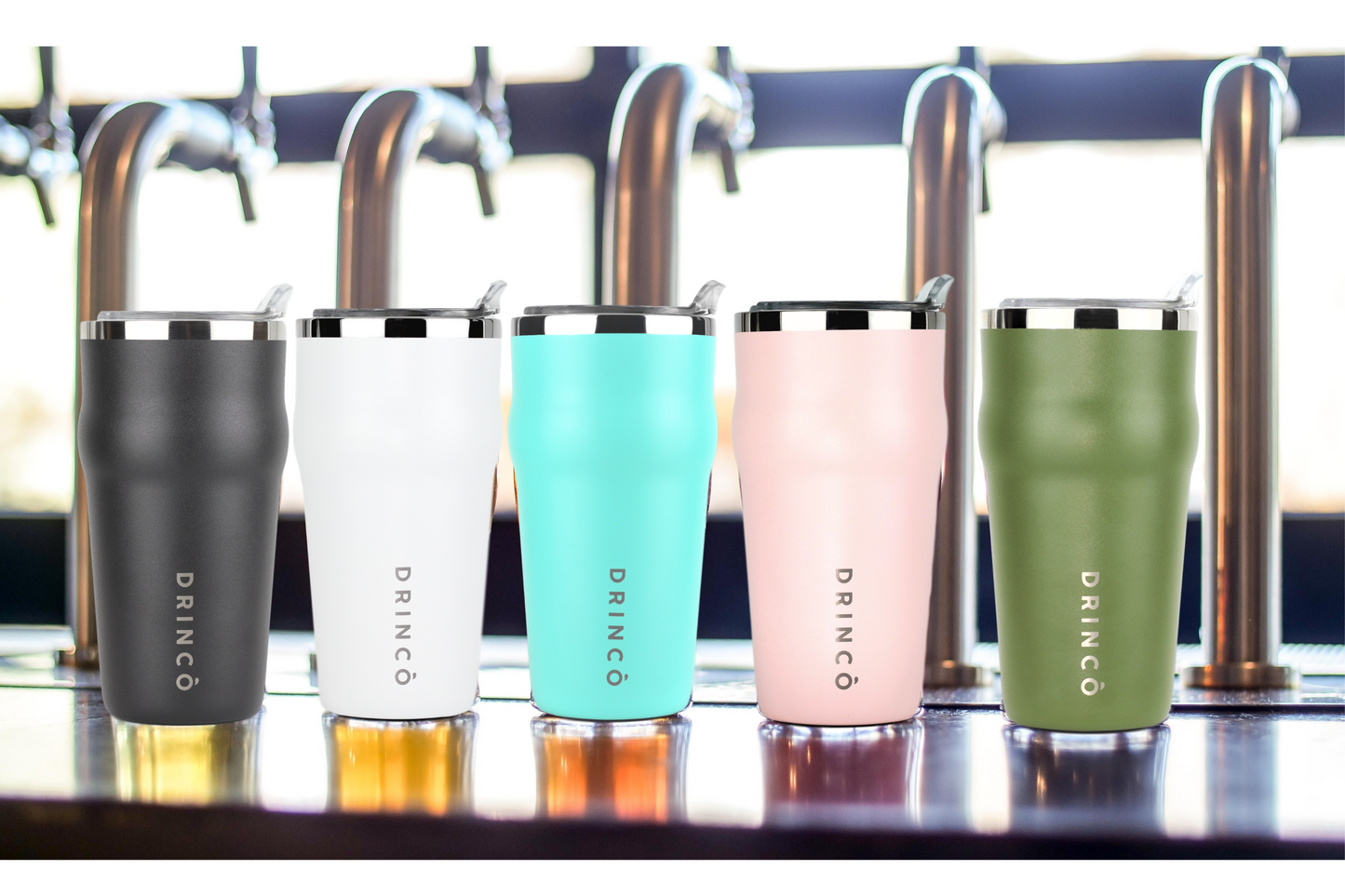 Five insulated tumblers in different colors on a bar counter with beer taps in the background.