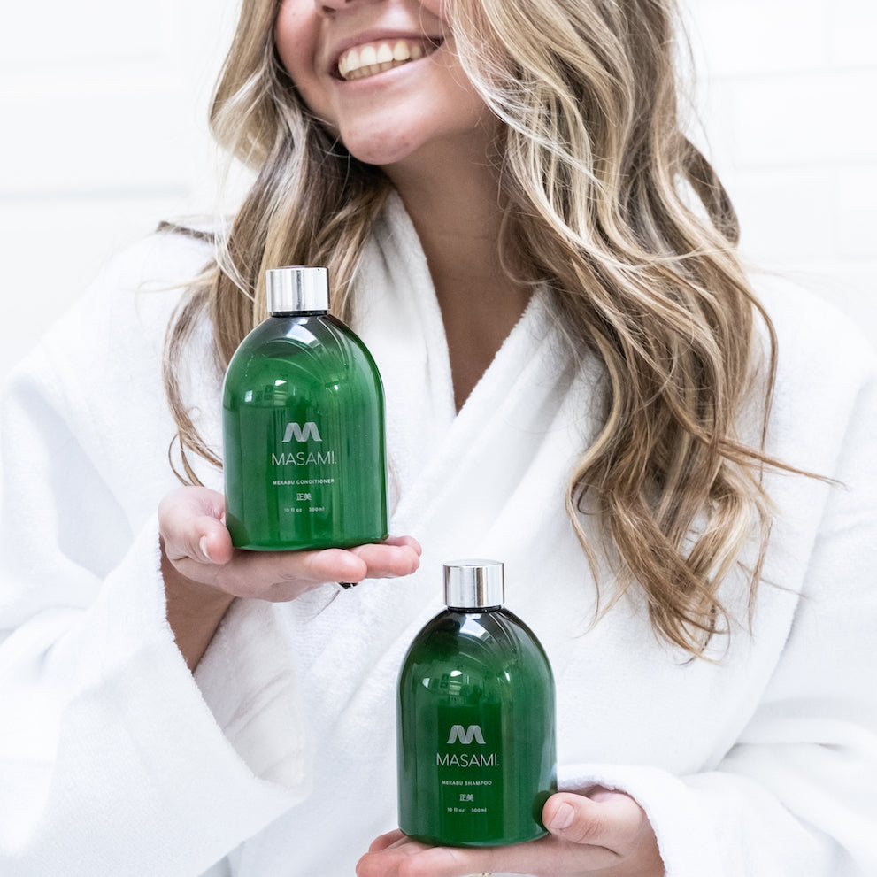 Woman in a white robe holding two green bottles labeled 'MASAMI' against a white background