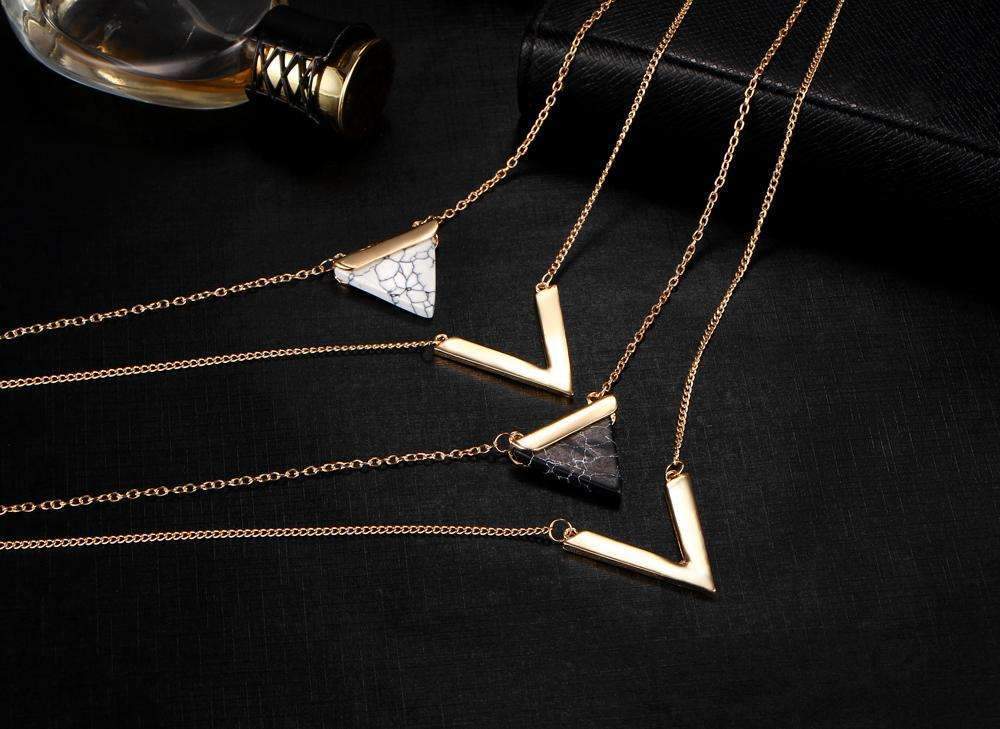 Two gold necklaces with geometric pendants on a black surface