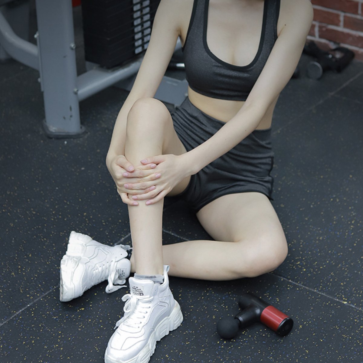 Person in athletic wear sitting on a gym floor with a dumbbell nearby