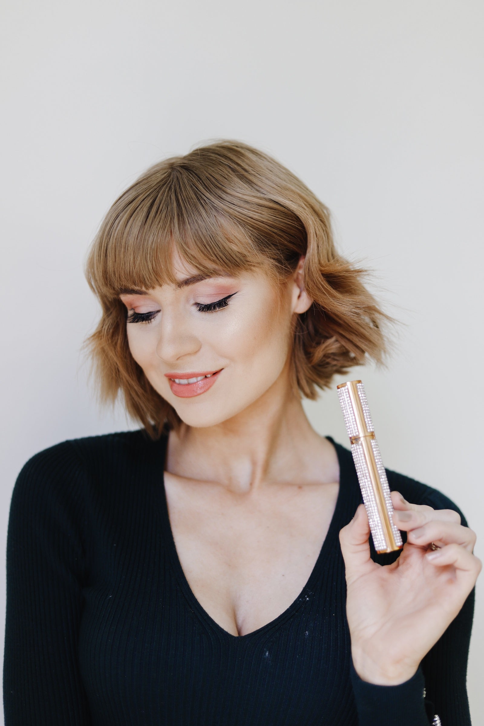 Woman holding a rose gold mascara wand against a plain background