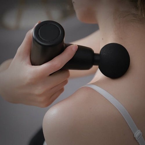 Person using a black handheld massager on their shoulder.