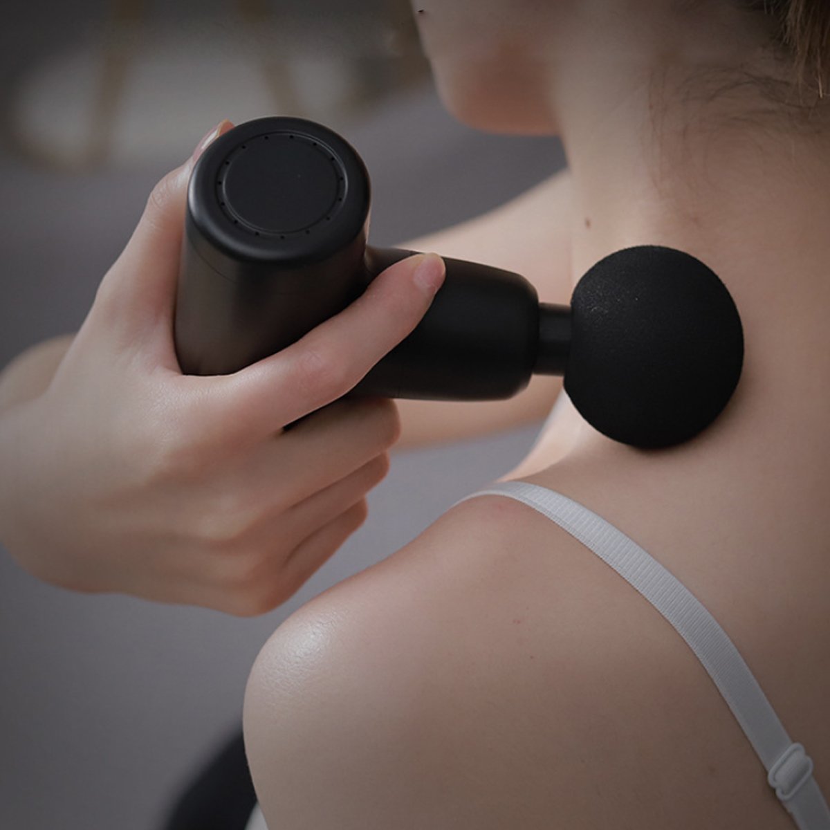 Person using a black massage gun on their shoulder