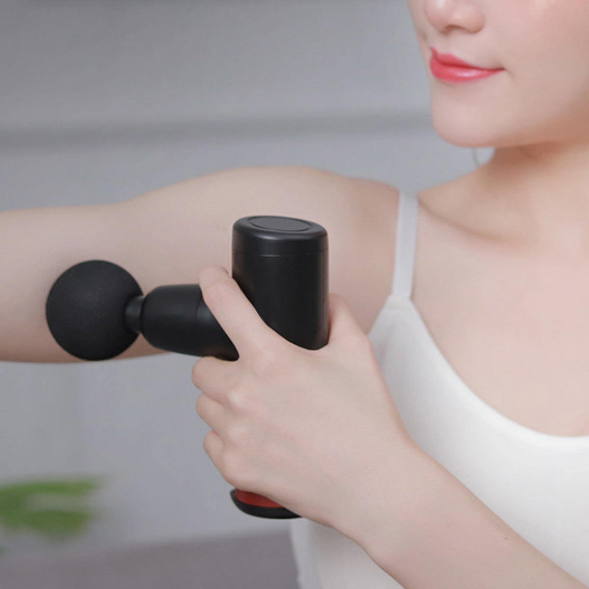 Person using a black handheld massager on their arm against a neutral background