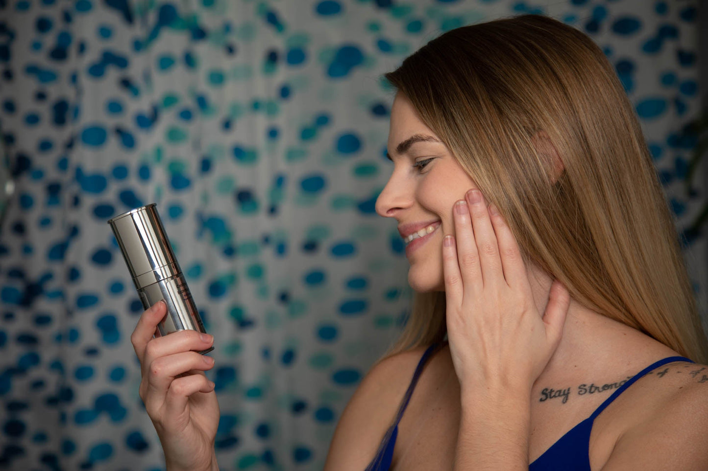 Woman applying a EpiLynx by Dr. Liia product to her face with a textured blue wall in the background