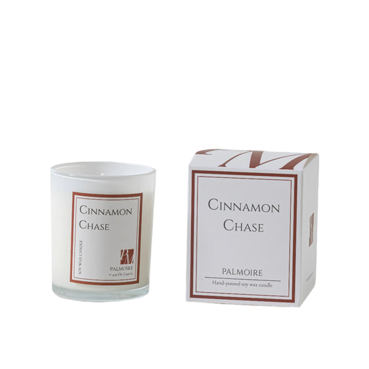 Candle labeled 'Cinnamon Chase' by Palmoire next to its packaging on a light background
