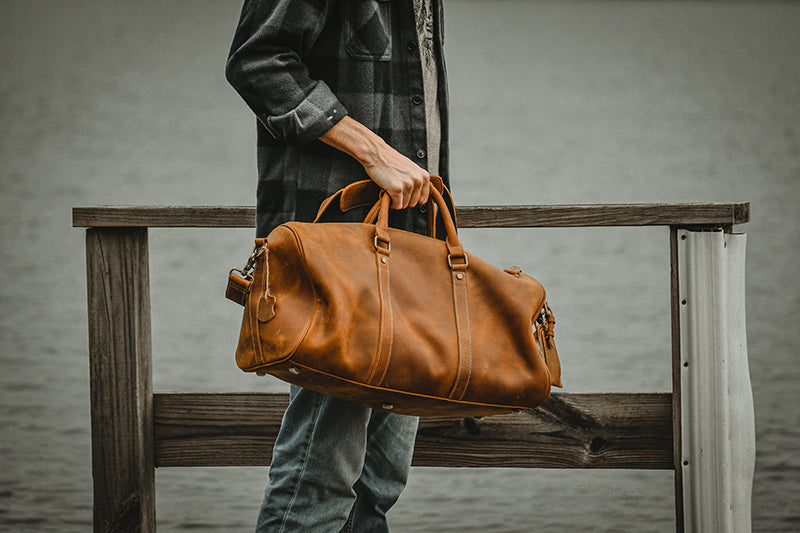 Person holding a brown leather bag on a wooden bench with a blurred background