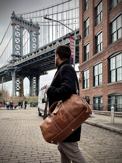 Man holding a brown leather bag in front of the Manhattan Bridge