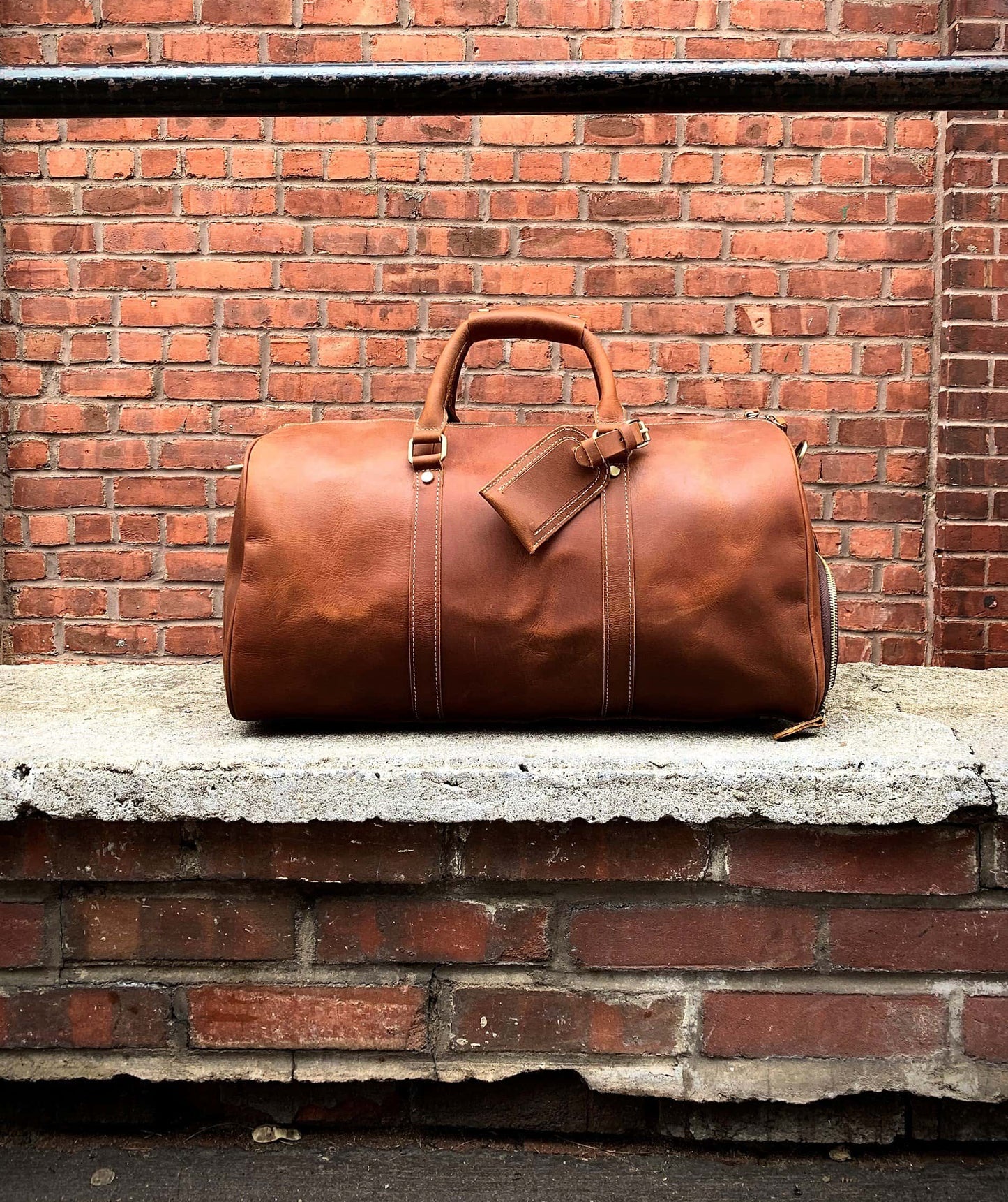 Brown leather duffel bag on a stone ledge against a brick wall.