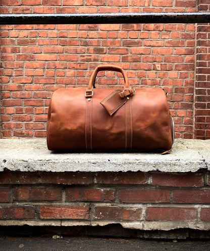 Brown leather duffel bag on a stone ledge against a brick wall.