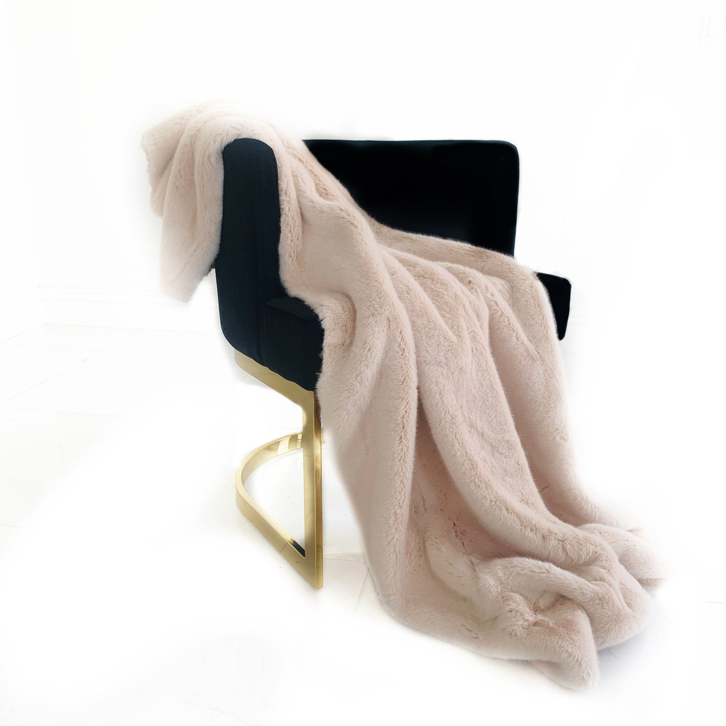 Black chair with a pink faux fur blanket draped over it on a white background