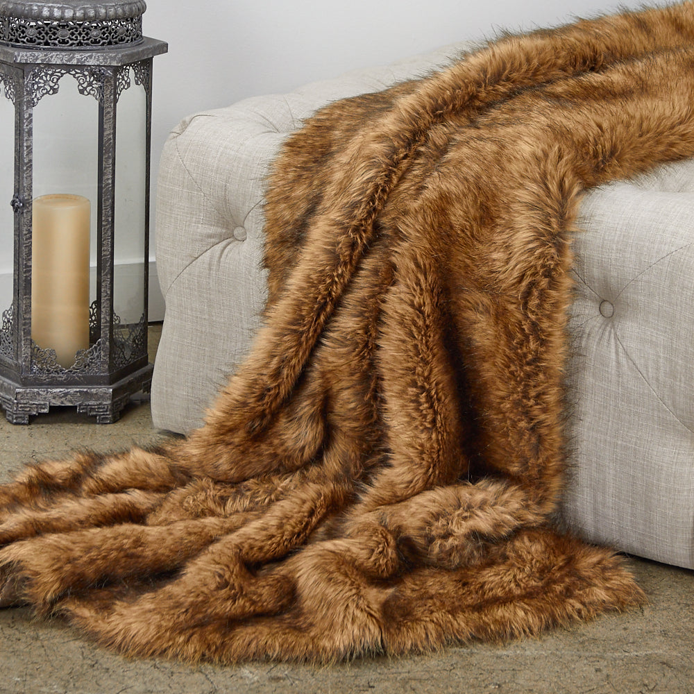 Brown faux fur throw blanket draped over a light gray sofa with a decorative candle holder in the background.