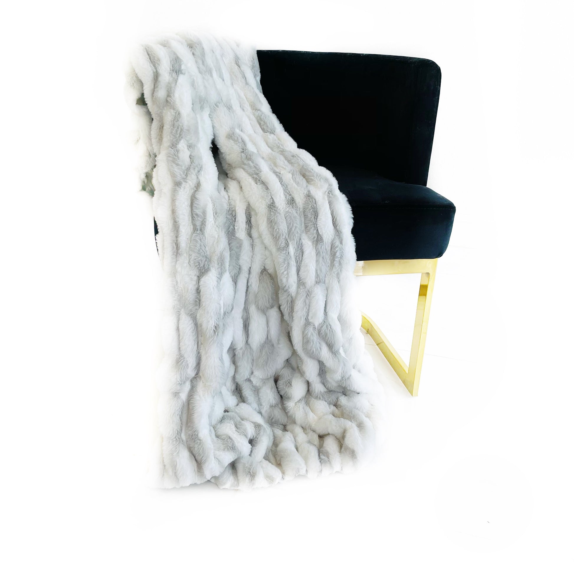 White faux fur throw blanket draped over a black chair with gold legs on a white background