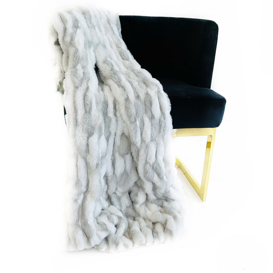 White faux fur throw blanket draped over a black chair with gold legs on a white background