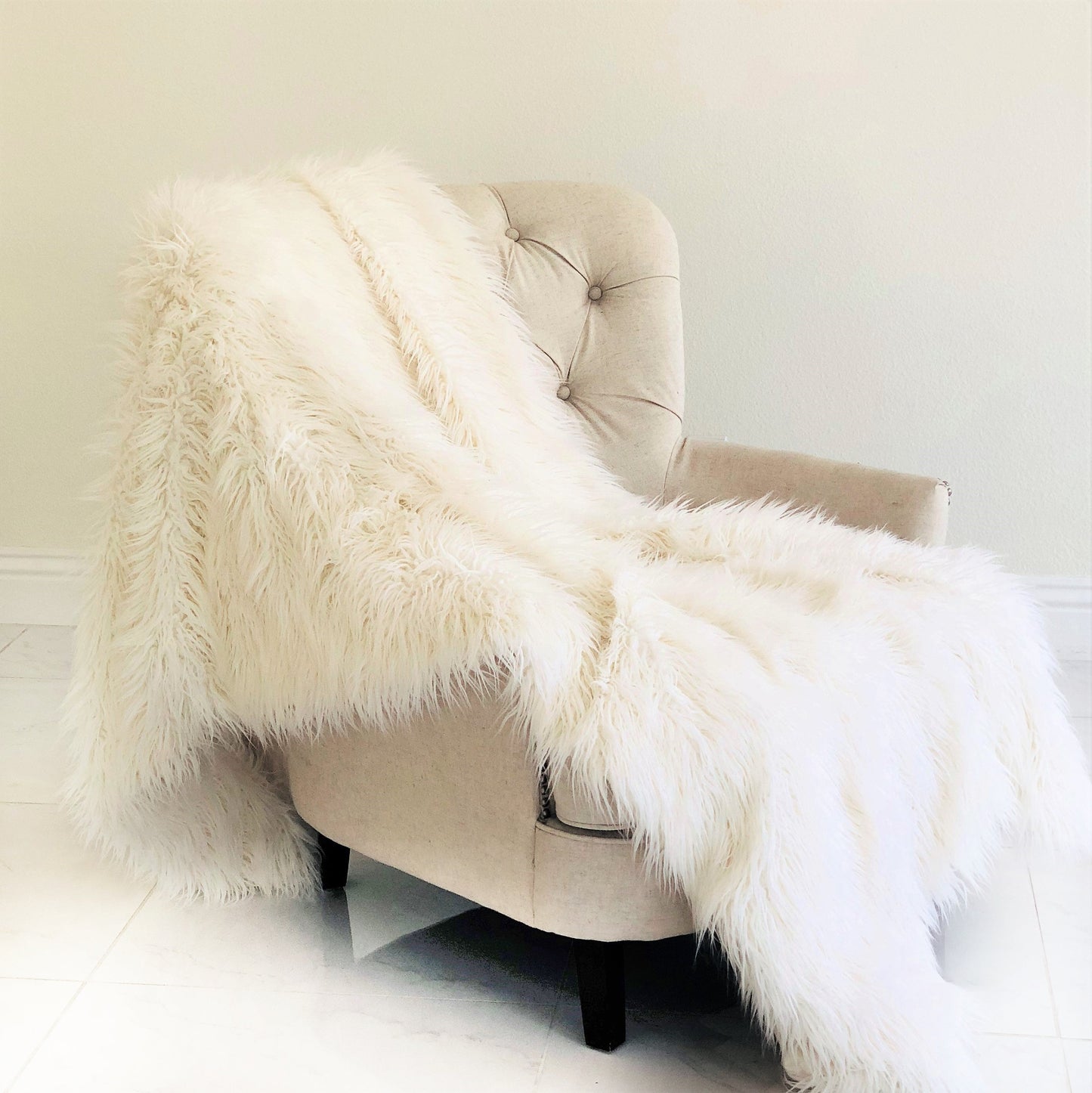 Beige armchair with a fluffy white throw draped over it against a plain wall.