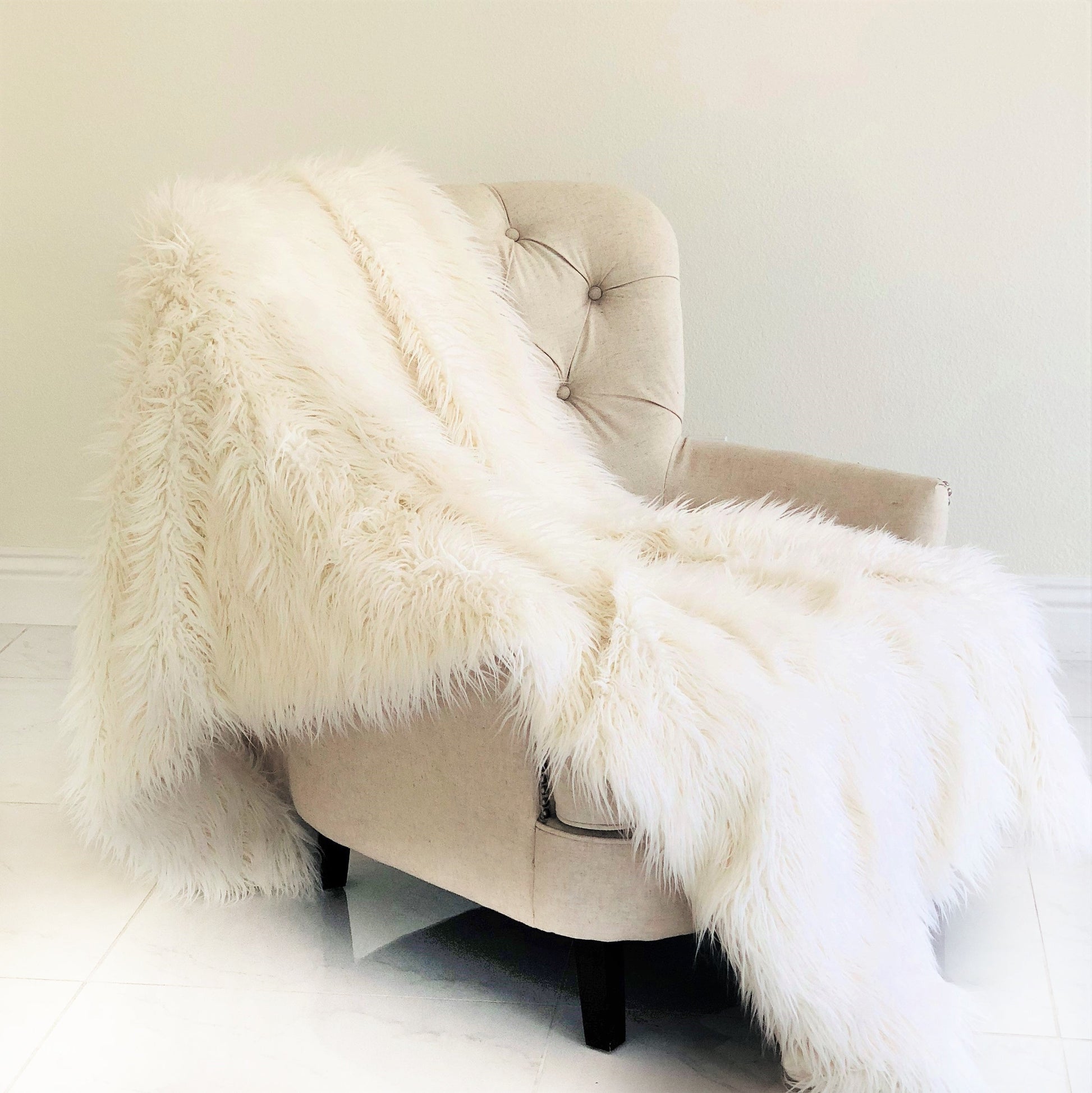 Beige armchair with a fluffy white throw draped over it against a plain wall.