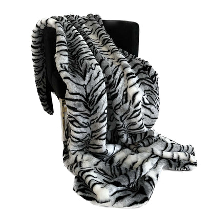 Zebra print faux fur blanket draped over a black chair on a white background