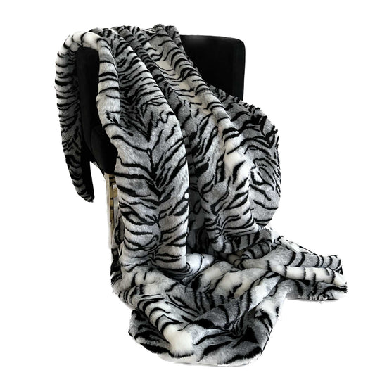 Zebra print faux fur blanket draped over a black chair on a white background