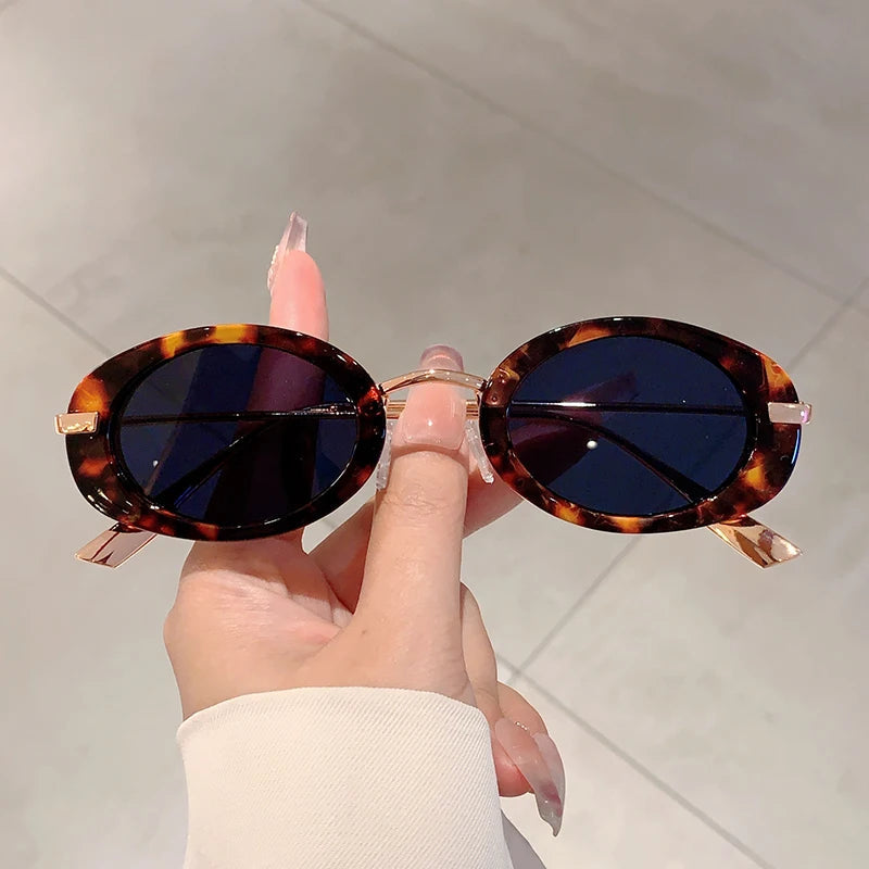 Hand holding a pair of tortoiseshell sunglasses with a neutral background