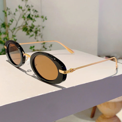 Round sunglasses with black lenses and gold frames on a white surface.