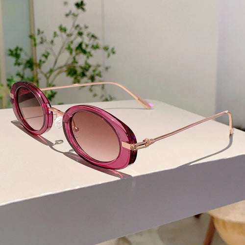 Pink sunglasses with gold frames on a white surface with a blurred green plant in the background