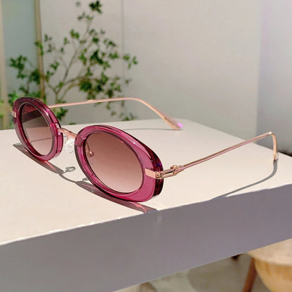 Pink sunglasses with gold frames on a white surface with a blurred green plant in the background