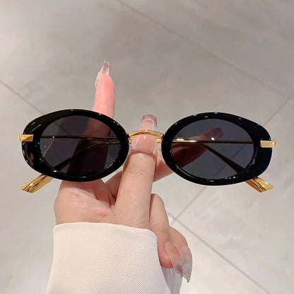 Black and gold sunglasses held by a hand against a light background