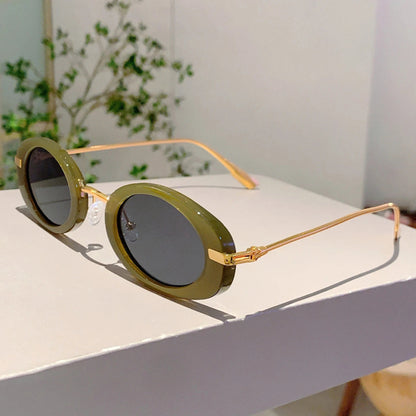 Sunglasses with green lenses and gold frames on a white surface with a plant in the background