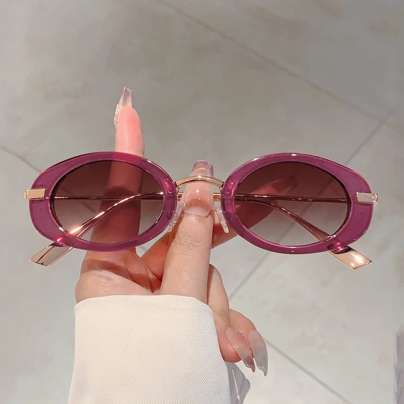 Pink sunglasses held by a hand against a neutral background