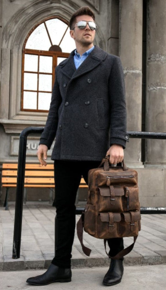Man in a dark coat holding a brown leather bag against an urban background