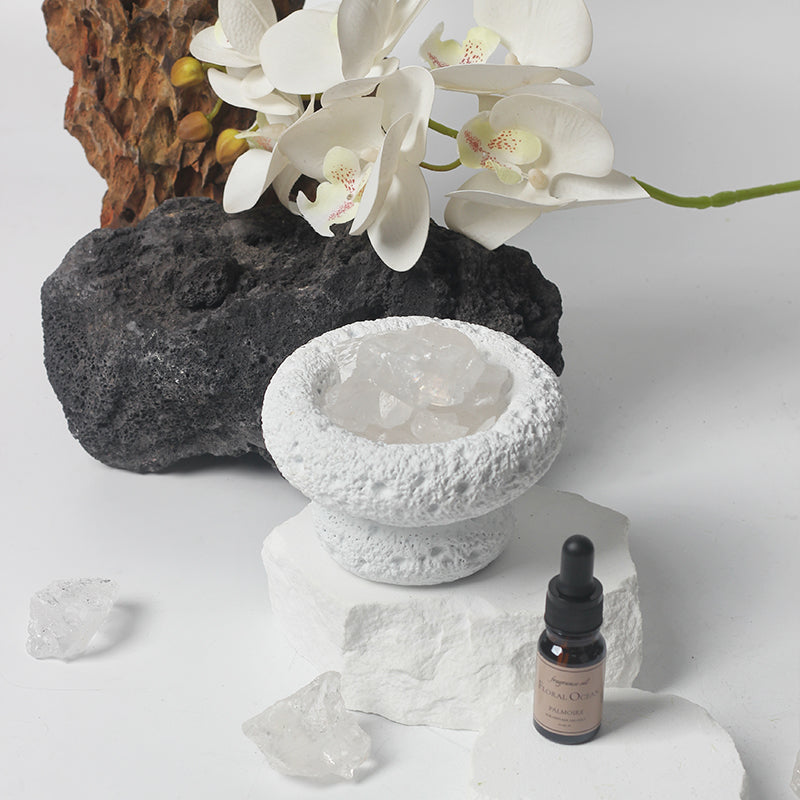 Ceramic bowl with Moon Quartz crystals, white orchids, and a bottle of Floral Ocean fragrance on a light background