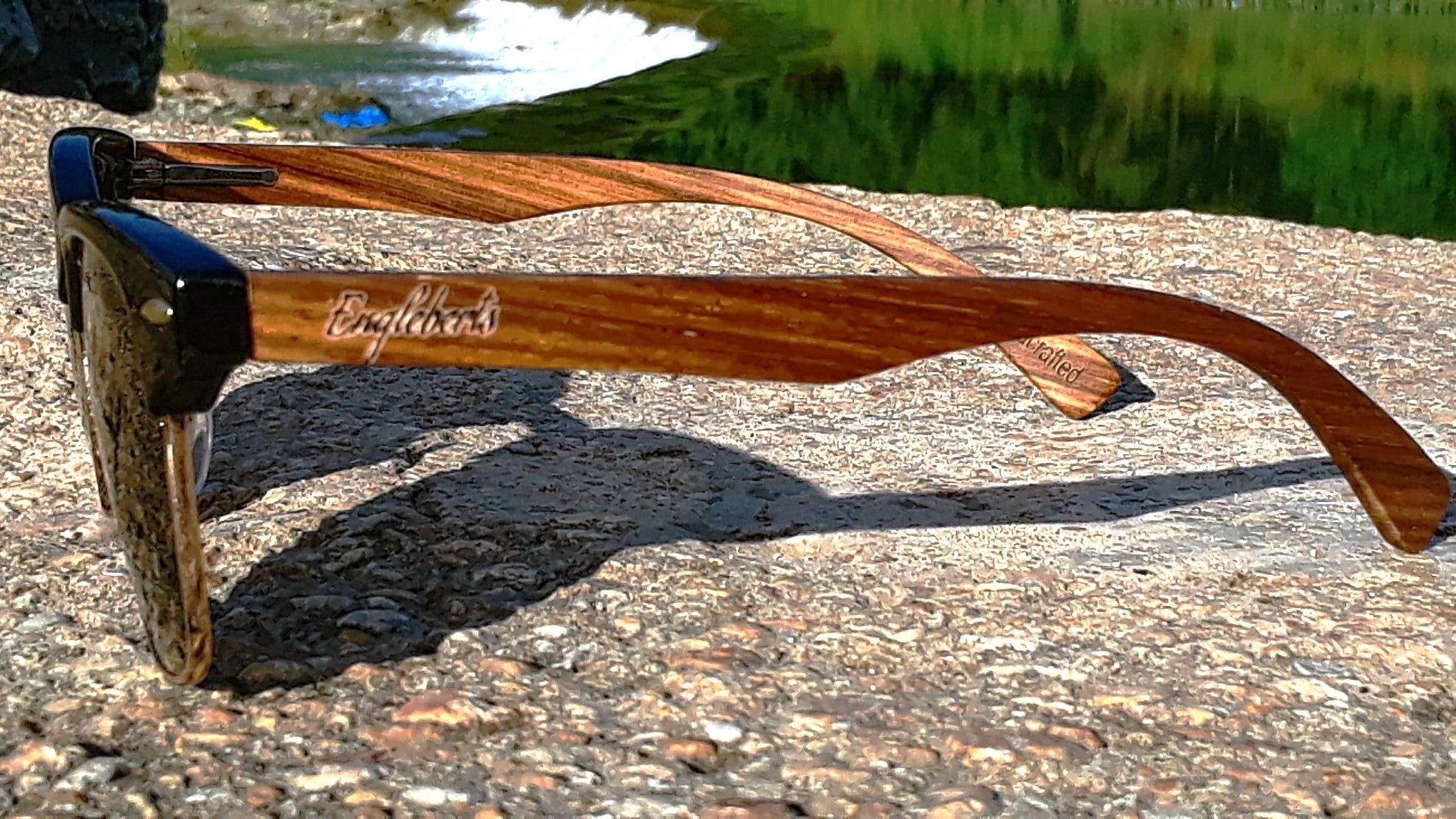 Wooden sunglasses with 'Beyonce' branding on a stone surface near water.