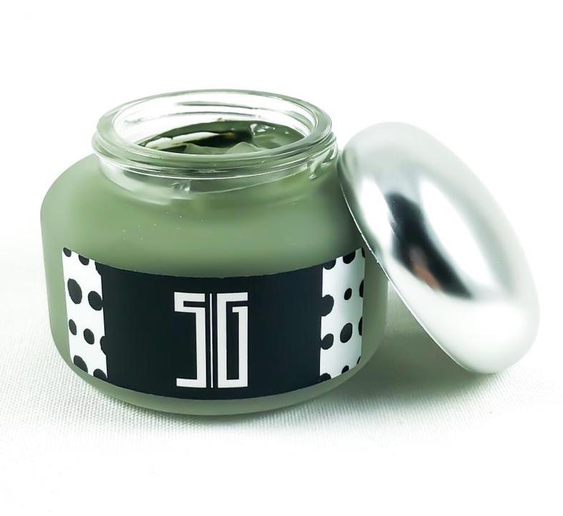 Jar of green cream with a black label and silver lid on a white background