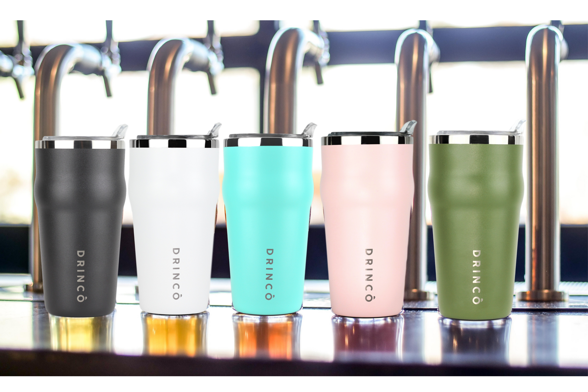 Five insulated tumblers in different colors on a bar counter with beer taps in the background.