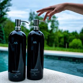 Two black bottles with silver pumps on a ledge by a poolside.