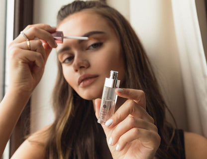 Woman applying makeup with a brush and bottle, indoors.
