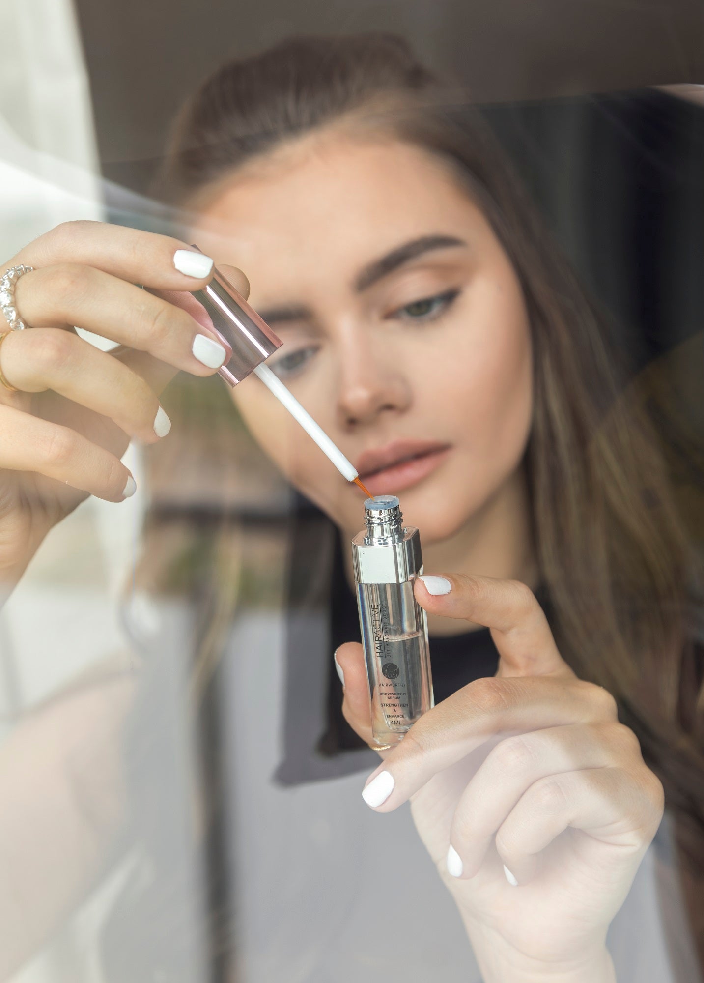 Woman applying makeup with a brush and bottle in front of a mirror