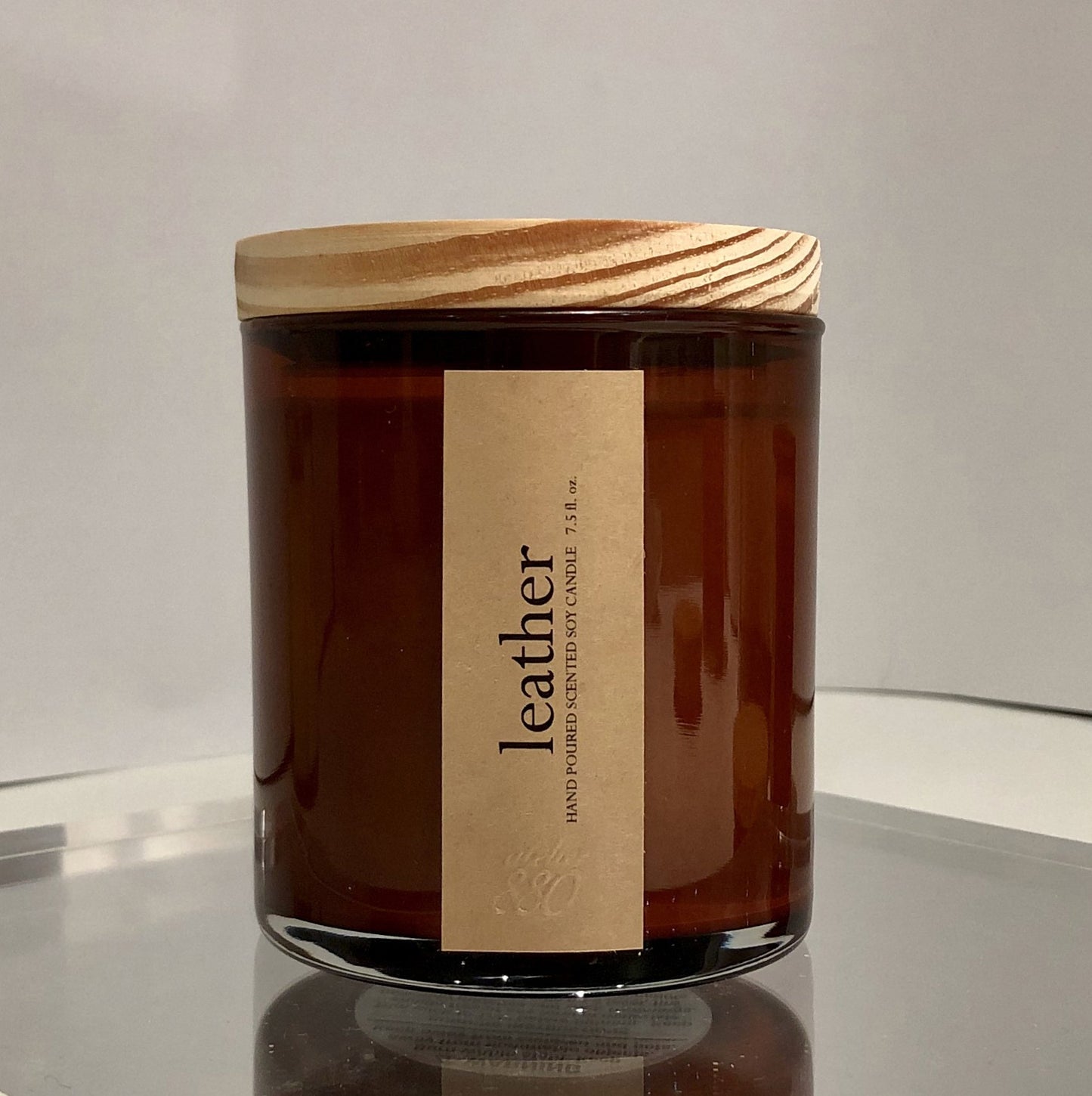 Brown candle jar, leather scent with wooden lid on a reflective surface