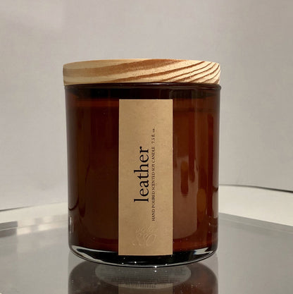 Brown candle jar, leather scent with wooden lid on a reflective surface
