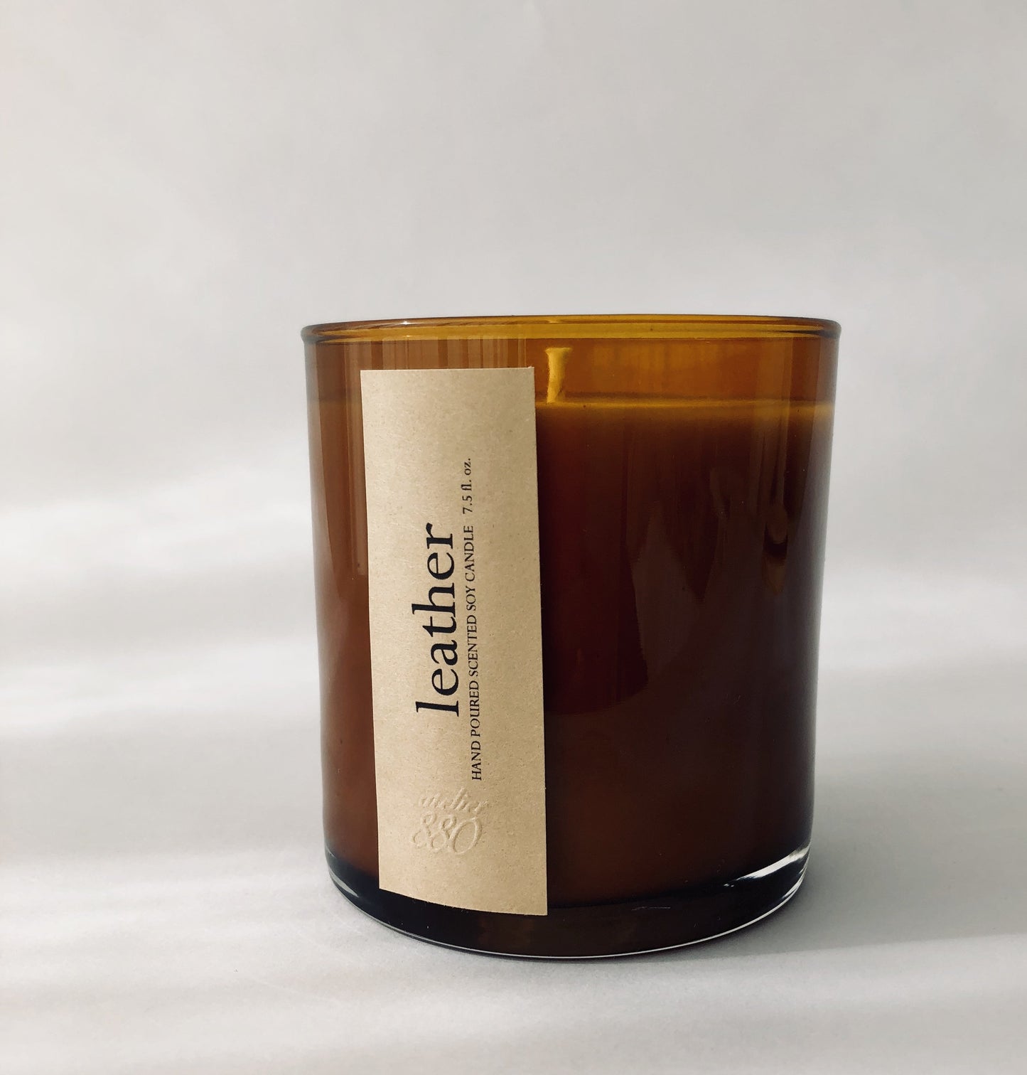 Brown candle with a label that reads leather hand poured scented soy candle on a white background