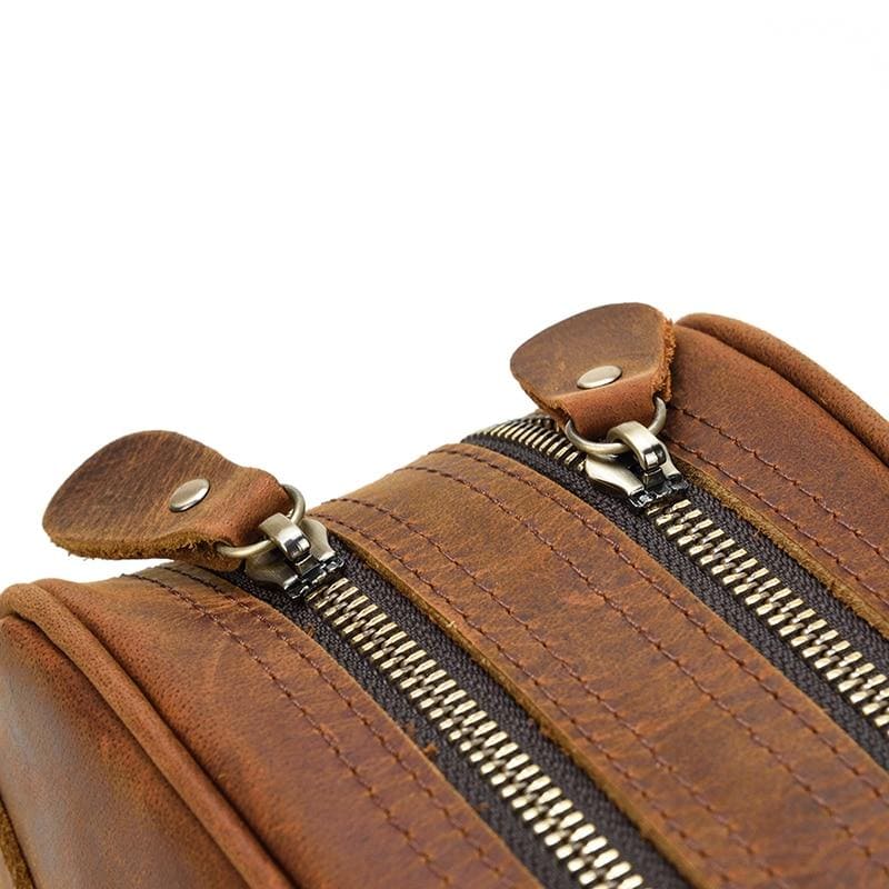 Close-up of a brown leather toilet bag with zippers on a white background