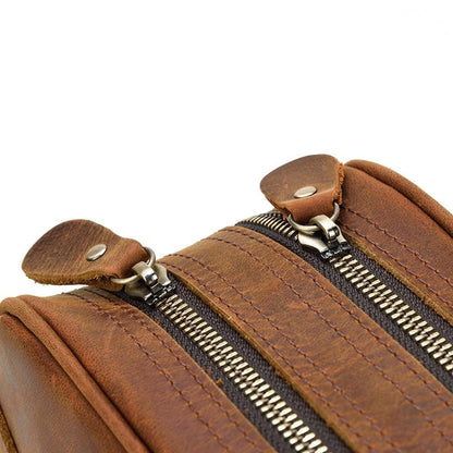 Close-up of a brown leather toilet bag with zippers on a white background