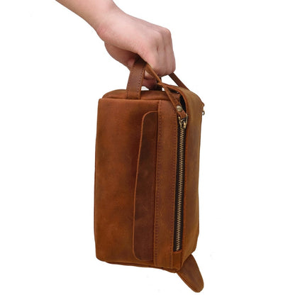 Brown leather toiletry bag held by a hand on a white background