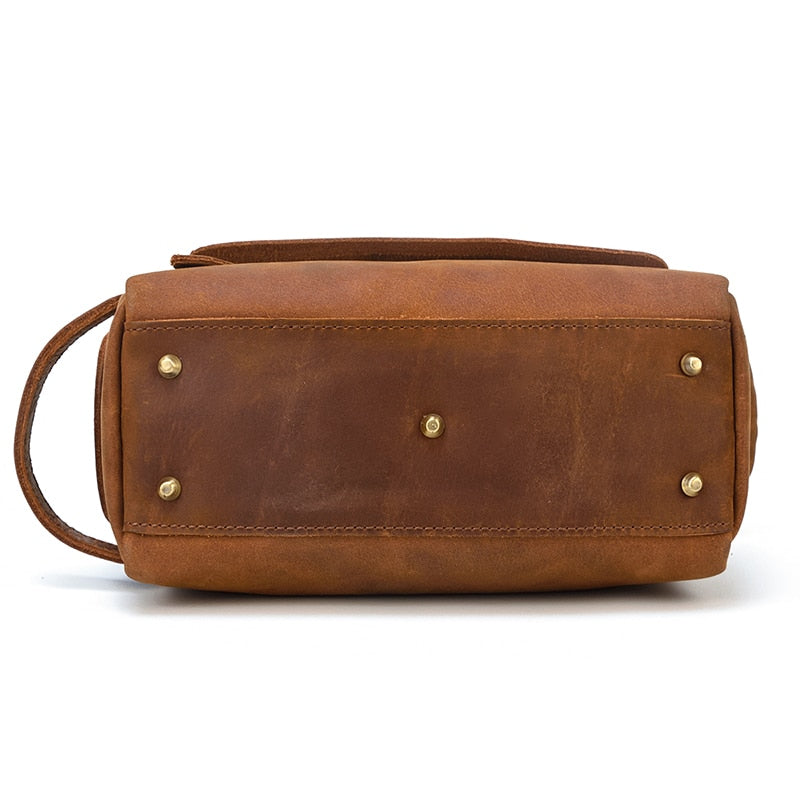 Brown leather toiletry bag with gold studs on a white background
