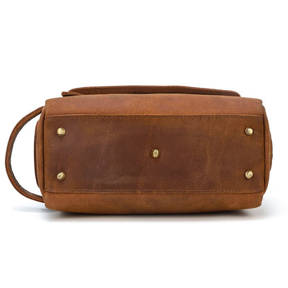 Brown leather toiletry bag with gold studs on a white background