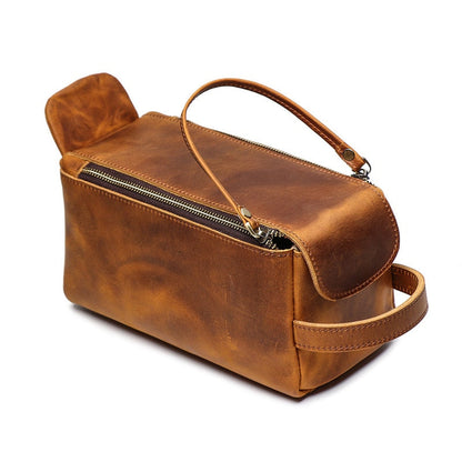 Brown leather toiletry bag with a handle on a white background