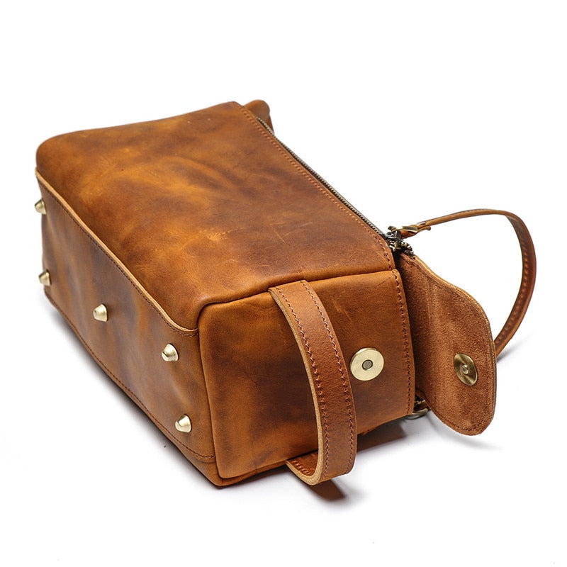 Brown leather toiletry bag with gold studs on a white background