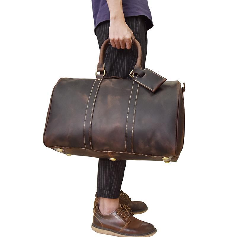 Person holding a brown leather duffel bag on a white background